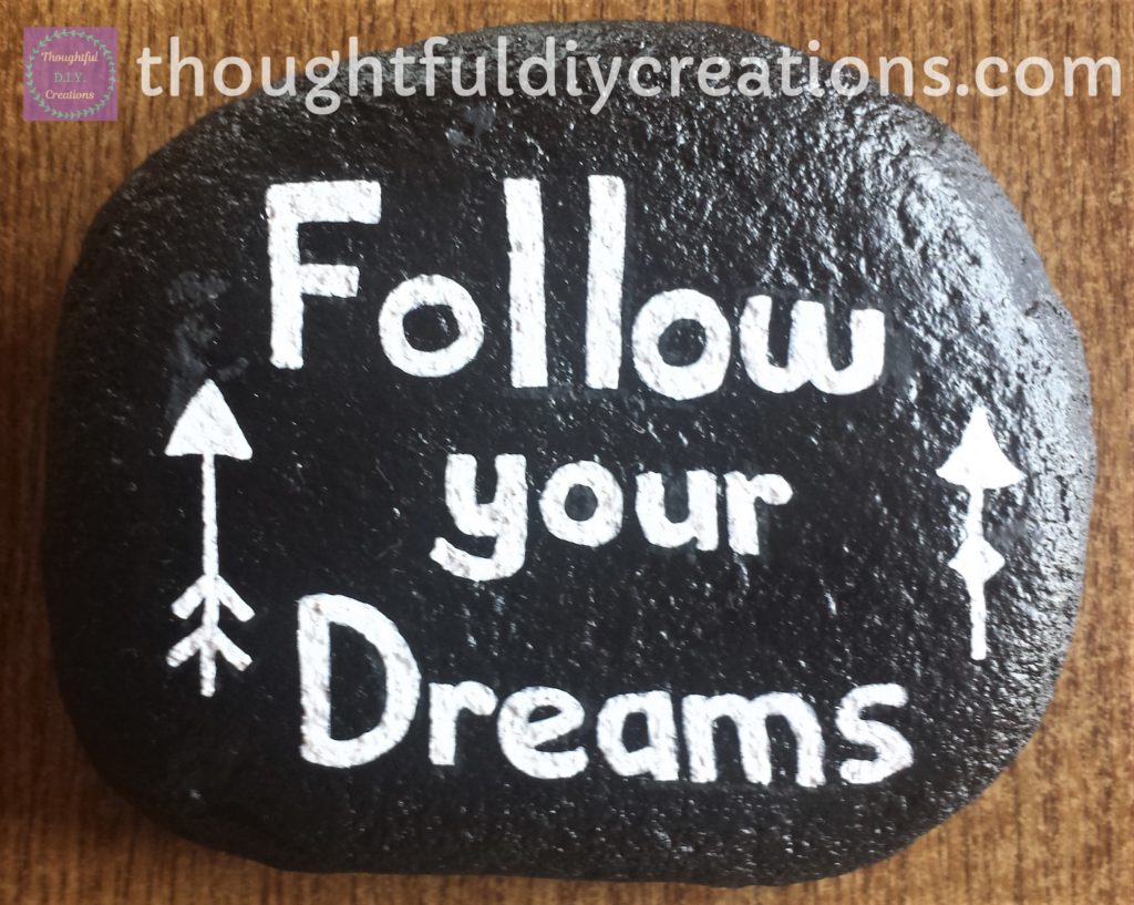 Black Spray Painted Stone with 'Follow your Dreams' Sentiment wrote on it with a white Paint Marker, and the arrows done with a white paint pen.