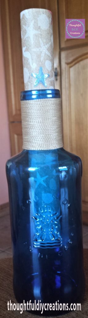 The beach themed sheet of paper rolled up and placed inside the blue glass bottle.