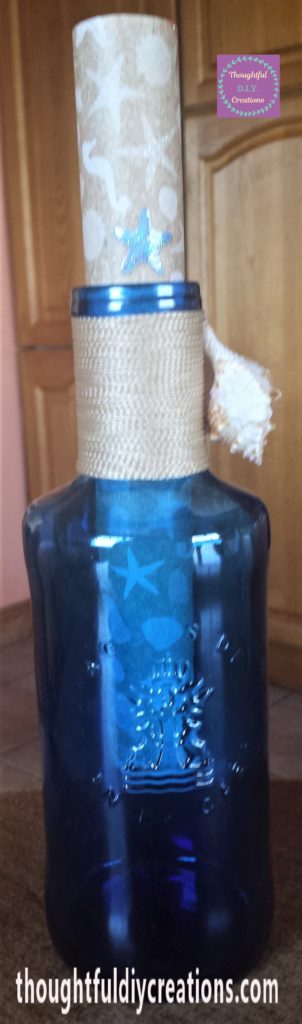 The small shell hot glued to the string at the side of the bottle.