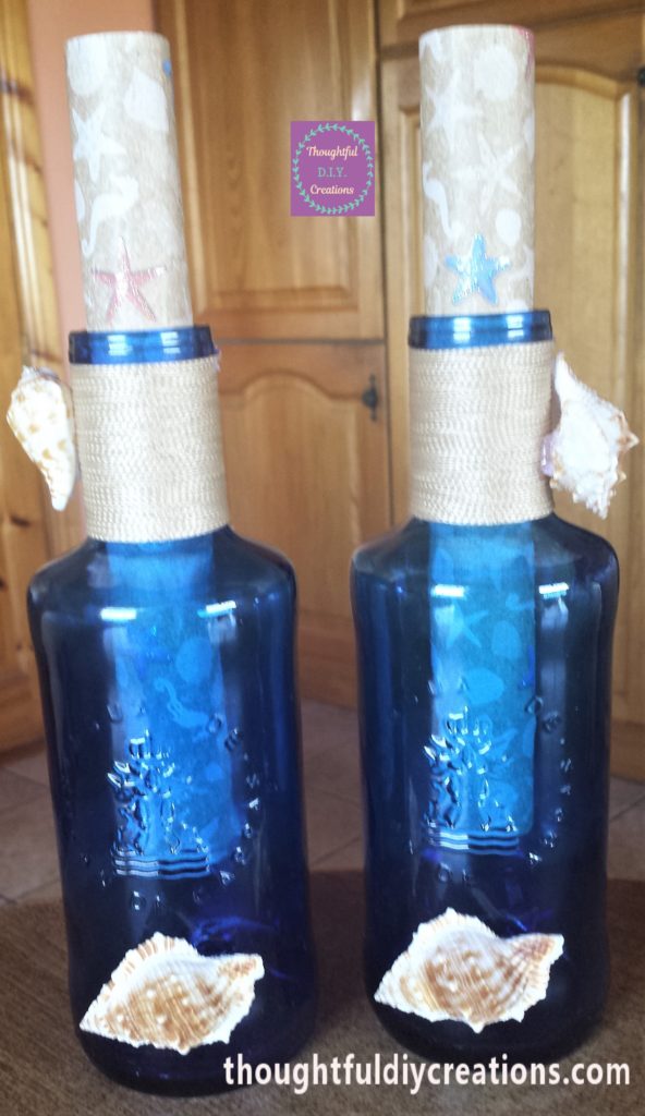 The two completed blue glass bottles transformed into Message in a Bottle beach themed D.I.Y. Craft.