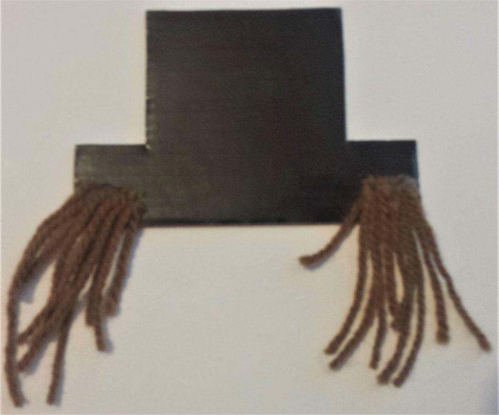 Attaching the wool strands to the back of each side of the hat with hot glue.