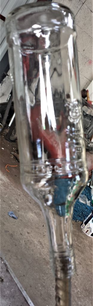 Bottle balanced on an iron bar in a watering can.