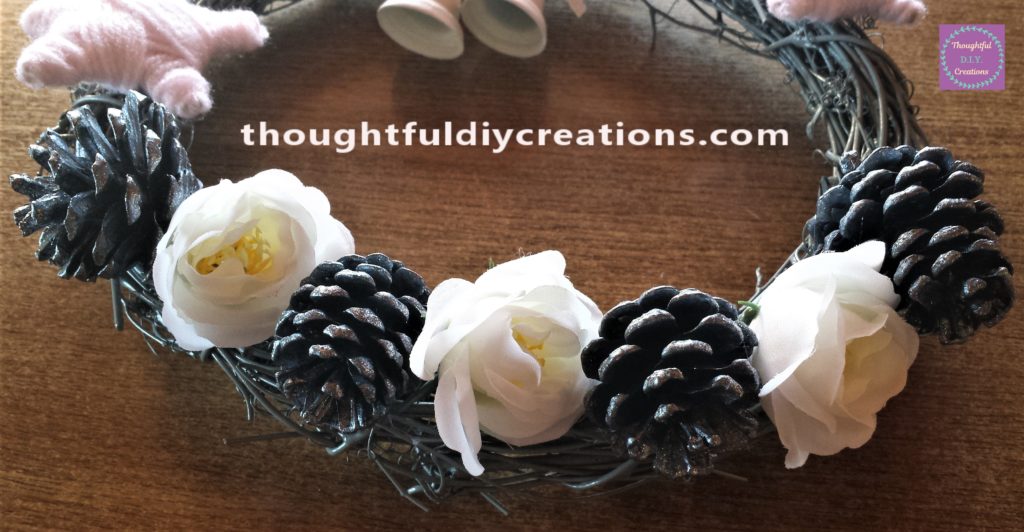 Close up image of 2 more pine cones and 1 more flower added to the wreath.