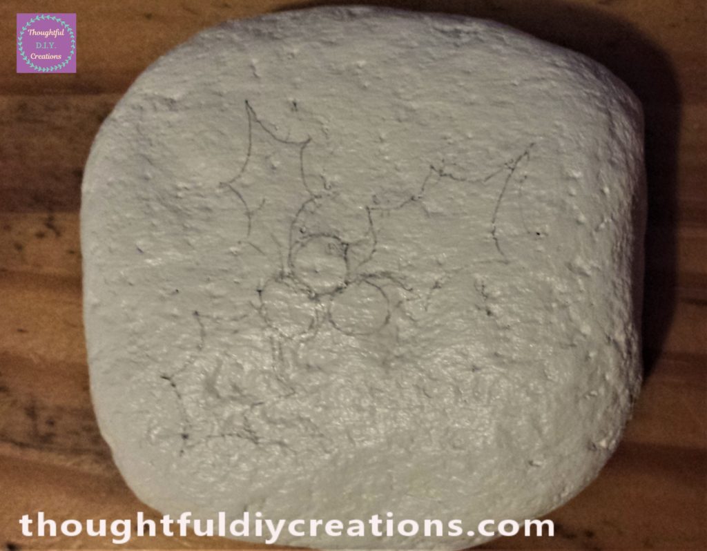 3 holly leaves and berries drawn onto the stone using a pencil.