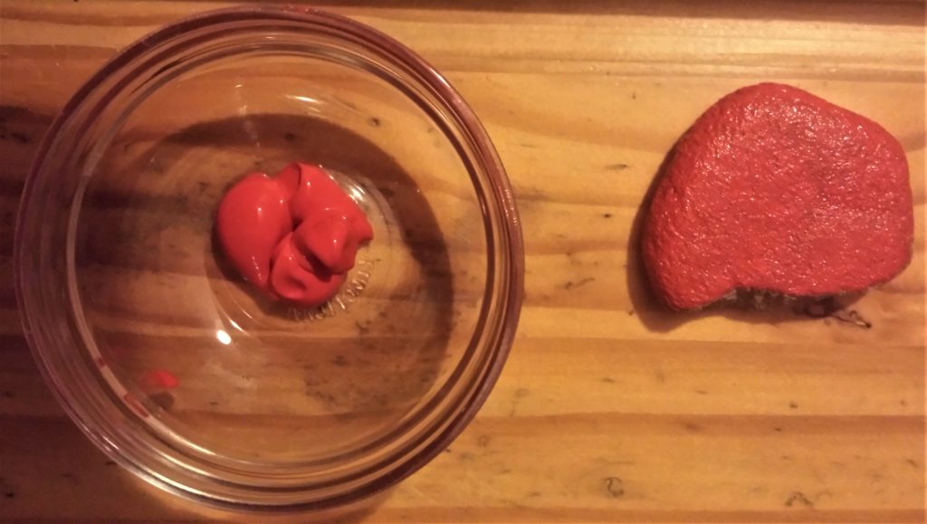 Red paint in a glass bowl, and first layer of paint on the stone.