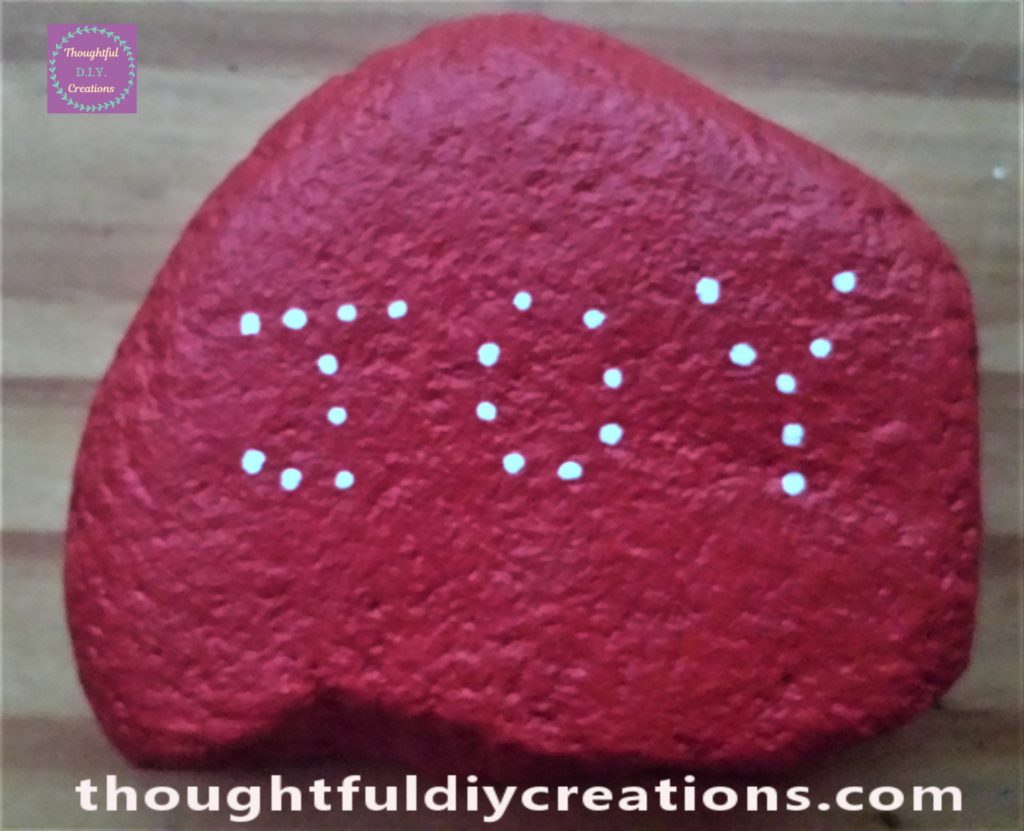 The word 'JOY' written on the stone in dots using a white paint pen.