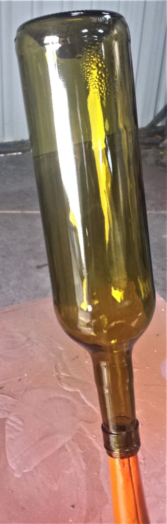 Wine Bottle balanced on the spout of a watering can on a table in the shed.