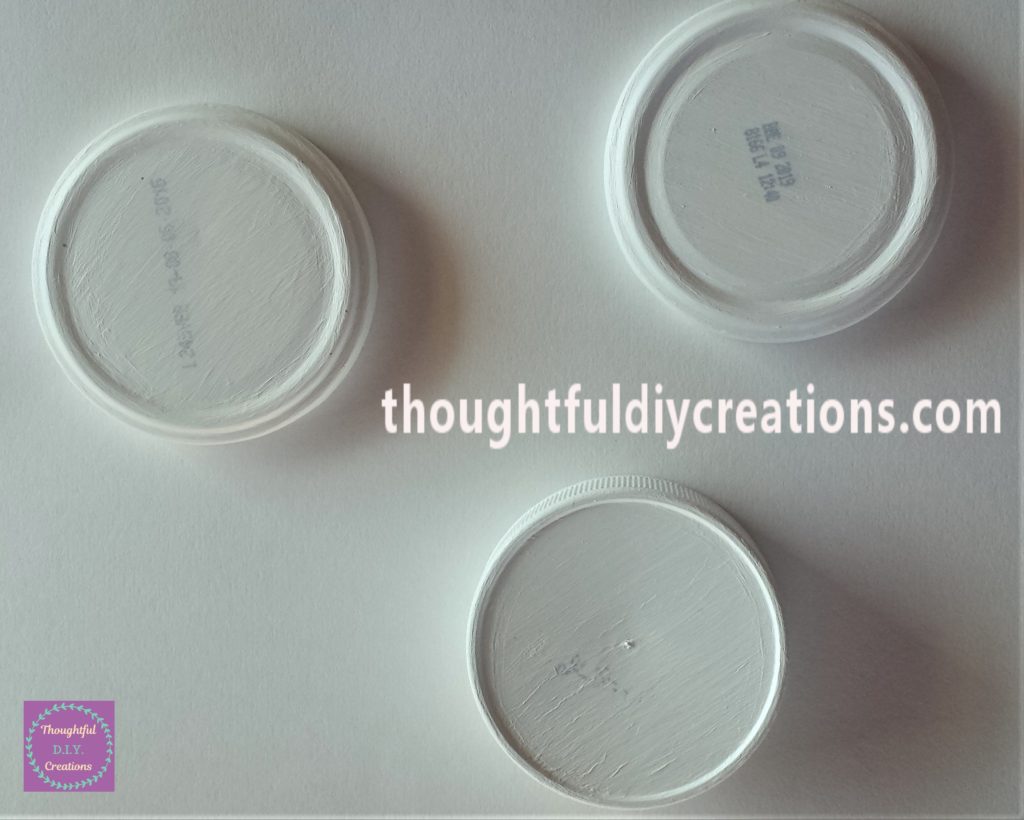 The 3 lids on a sheet of white cardstock on the table.