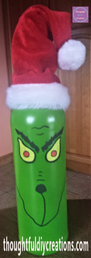 The outline of the red part of the Grinch's eyes done with a black paint pen. The Santa hat placed on top of the bottle.
