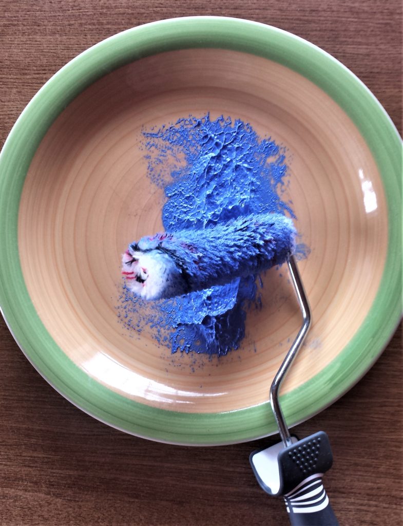 Blue paint on a plate with the roller dipped into the paint.
