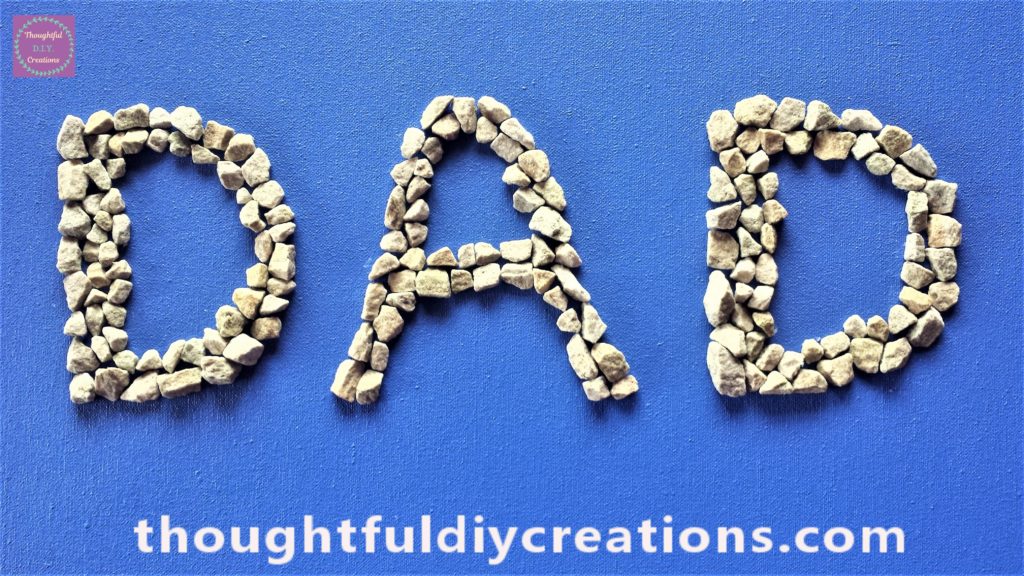Close up image of the word 'DAD' spelled out on the canvas board with stones.