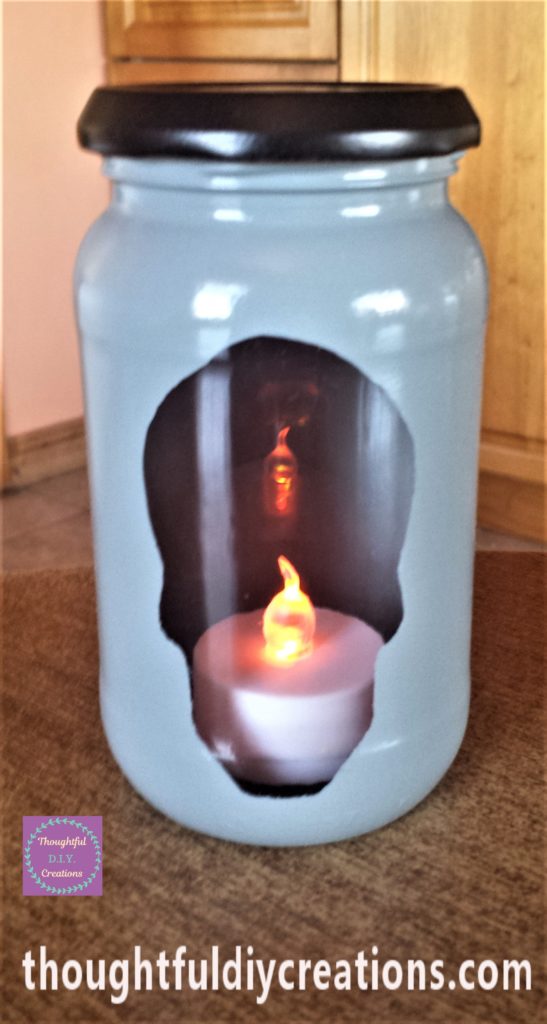 The spray paint around the edge of the skull carefully removed with a baby wipe. An LED colour change t-light candle in the jar with the lid on.