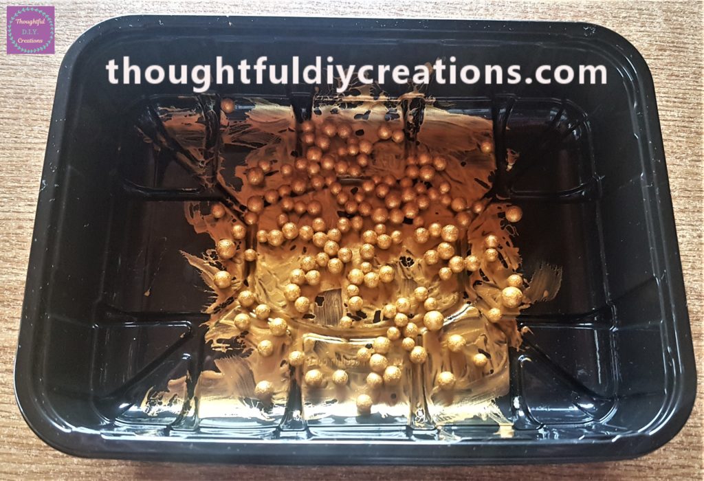 The mini glitter balls in a plastic container covered with gold acrylic paint.