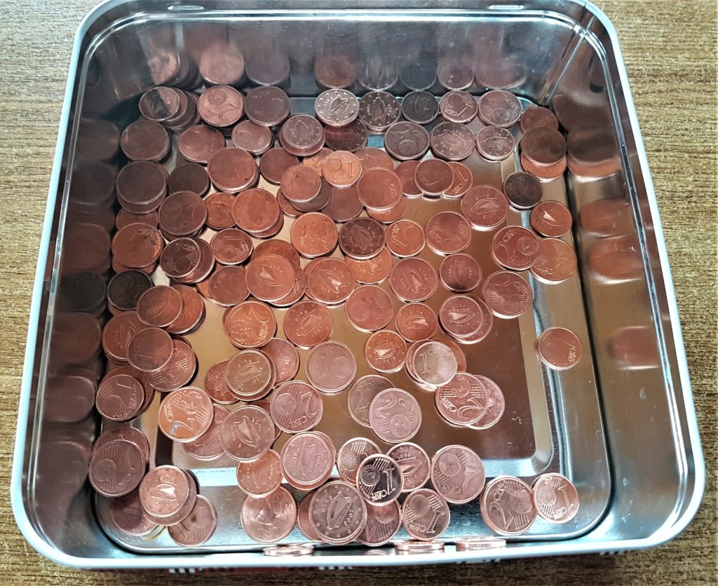The coins in a container after being soaked and washed in the sink with a cloth.
