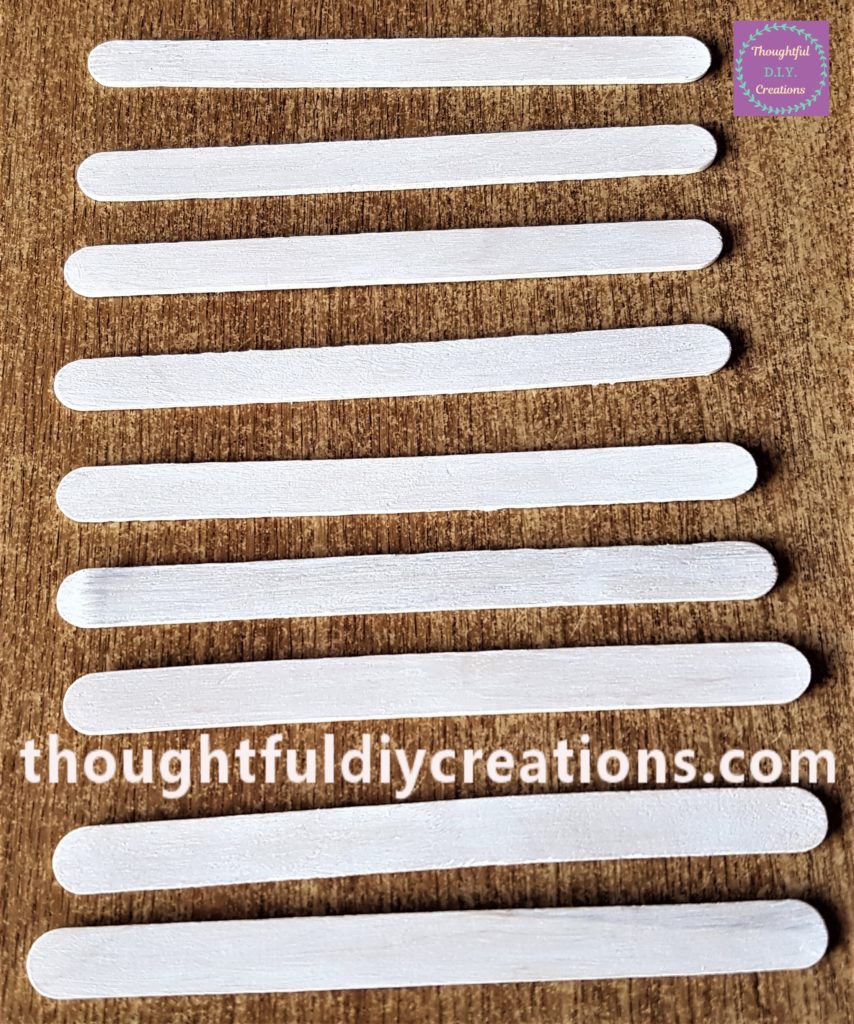 9 Lollipop sticks painted with white acrylic paint and a small paintbrush.