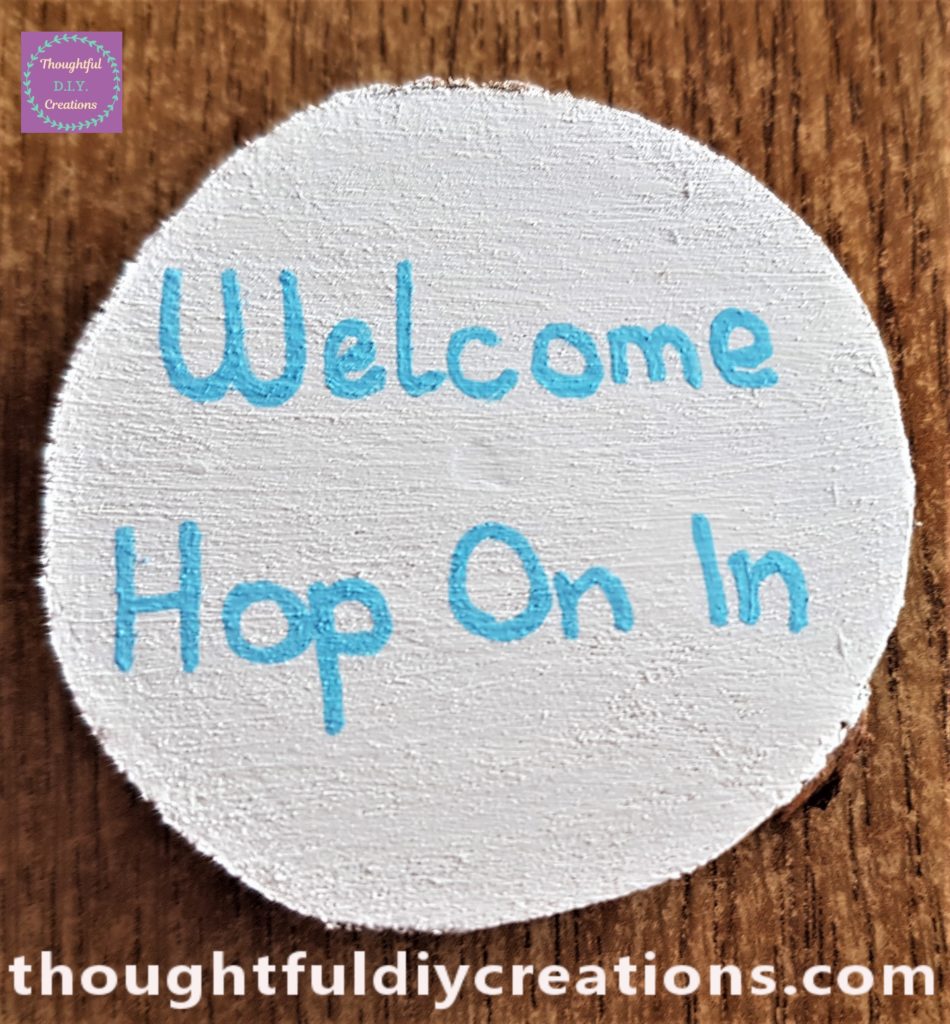 'Welcome Hop On In' wrote on the white painted wood slice with the blue paint pen.
