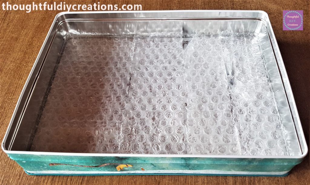 PVA Glue spread all around the inside of the biscuit tin and the bubble wrap pressed into it until the first layer was filled.