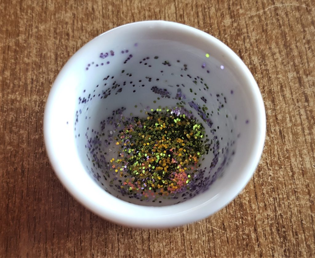 Purple and green glitter poured into a small glass container.