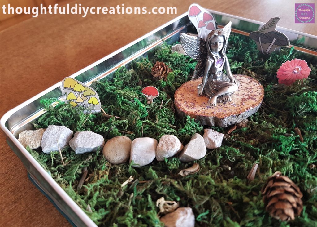 The glitter wood slice back in the Fairy Garden with the Fairy on top of it.