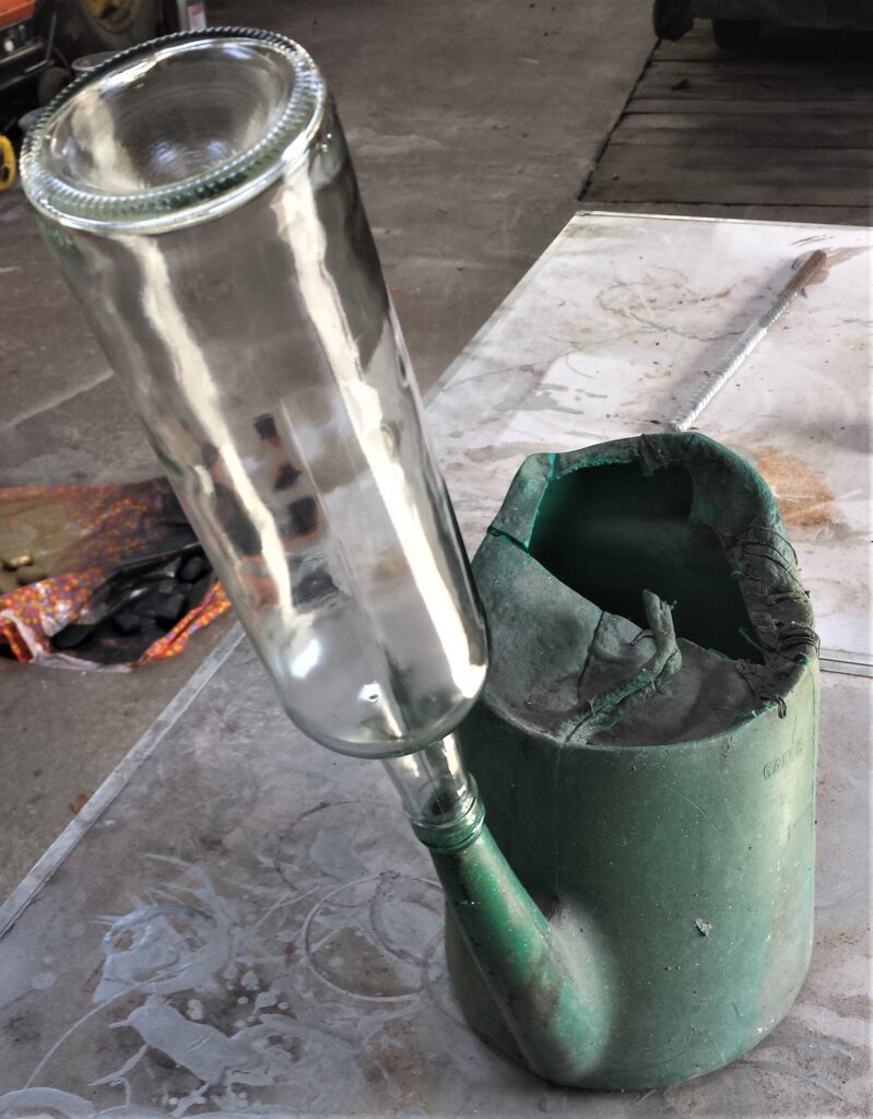 Wine bottle balanced over the spout of an old watering can.