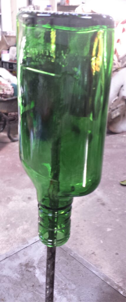 Iron Bar through a hole in a Crate. The bottle balanced over the iron bar to keep it in place.