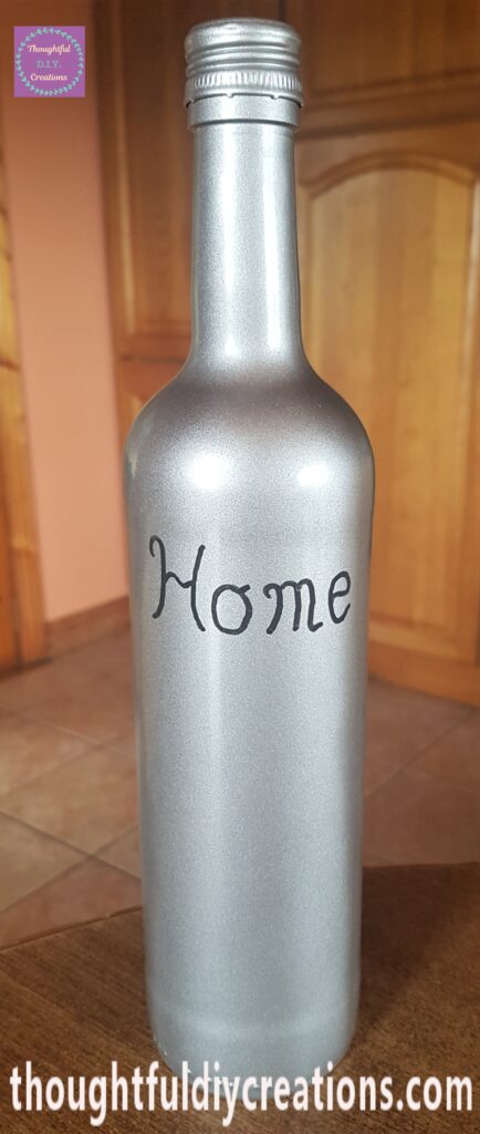 The word 'Home' written on the bottle with the paint marker in a slightly curved text.