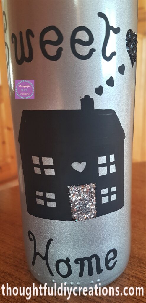 PVA Tacky Glue spread over the heart on the bottle, black glitter poured over the glue. Glue spread over the door of the house, silver glitter poured over the glue.