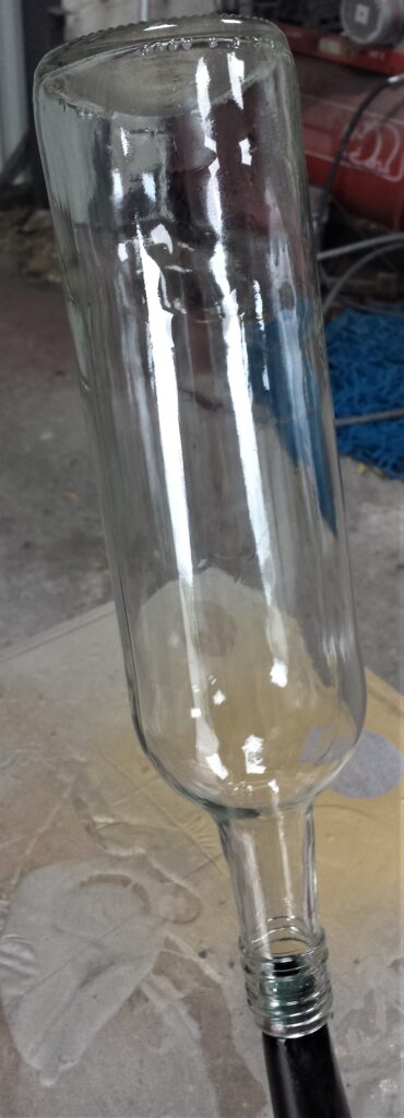 Top of wine bottle over the spout of an old watering can.