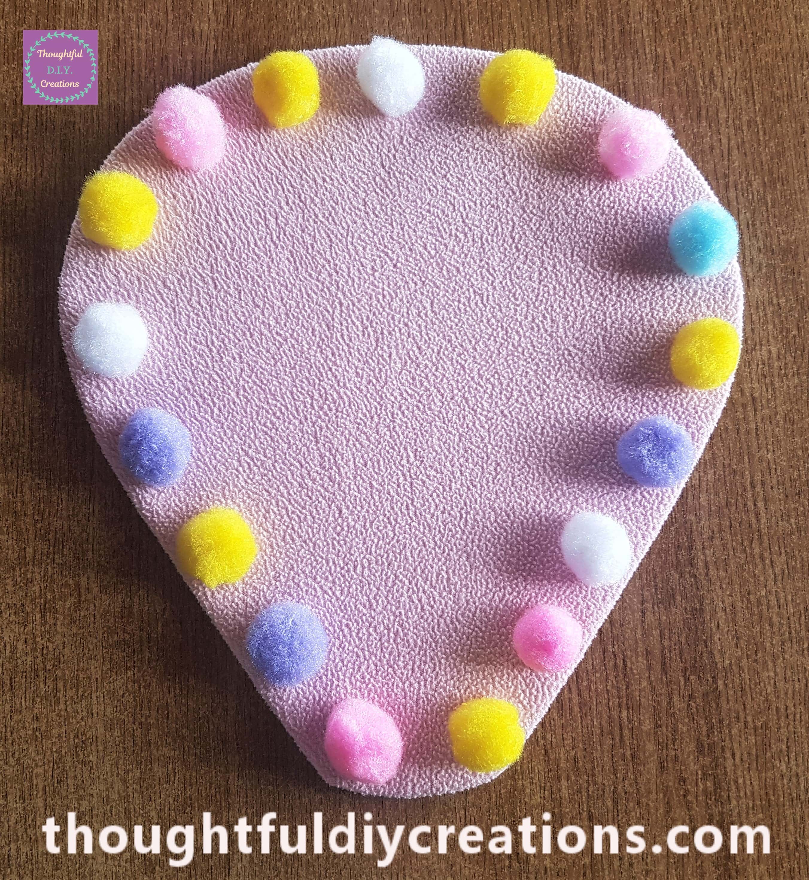 Biggest Pom Poms separated evenly around the edge of the Hot Air Balloon and hot glued on.