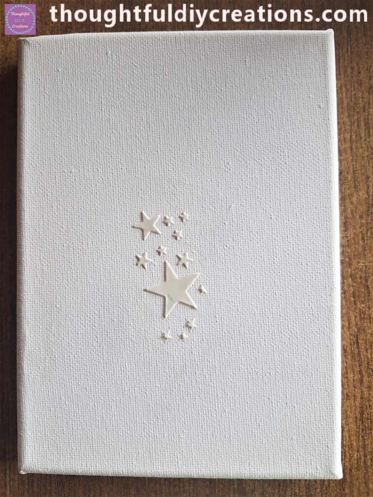 Plastic Palette Knife dipped into modeling paste, stencil in the middle of the canvas, spread the modeling paste over the stars on the stencil with the palette knife.