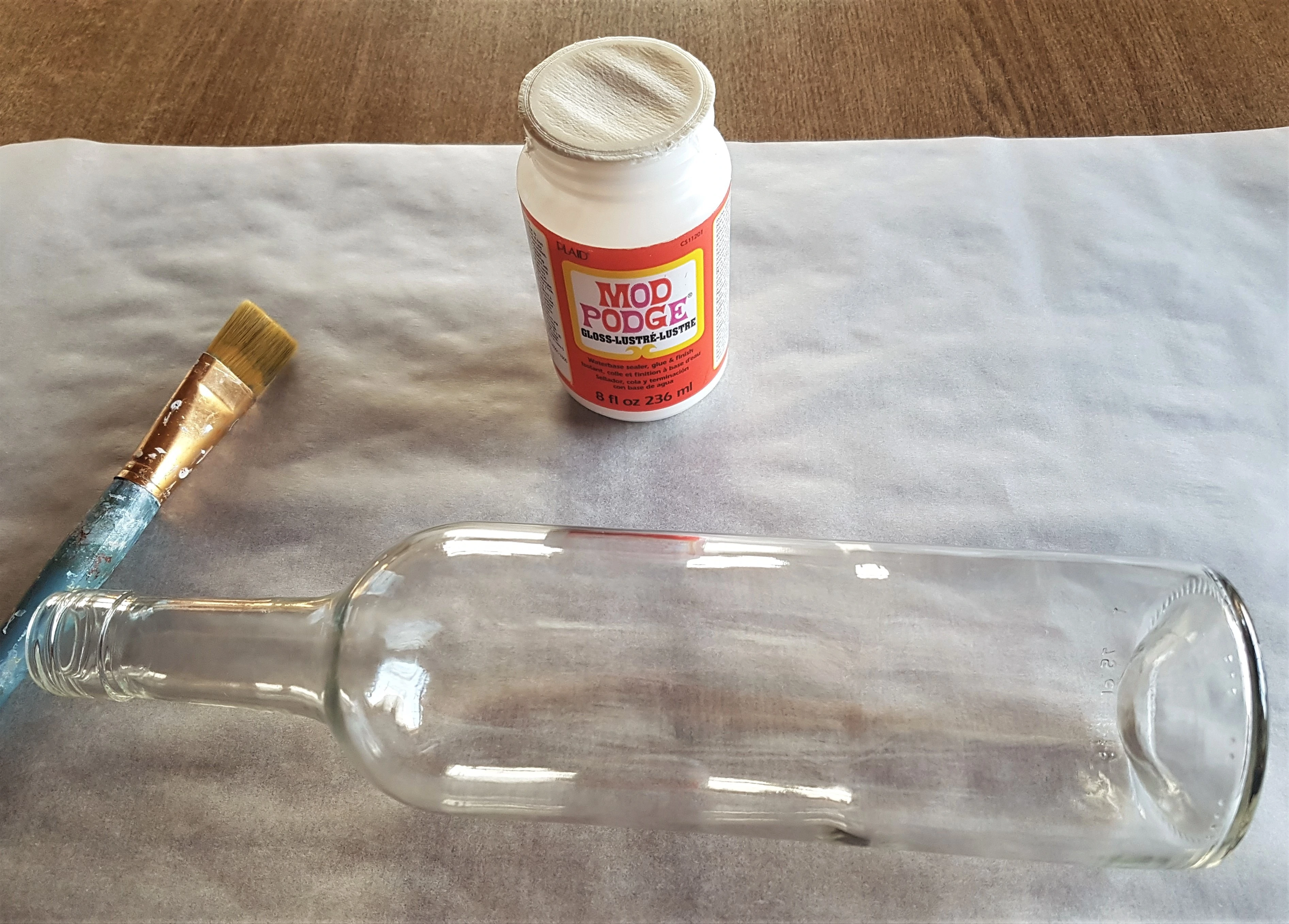 Baking Parchment Paper on the Table. Mod Podge Gloss and Flat Paintbrush. I put the Wine Bottle lying down on the Baking Paper.