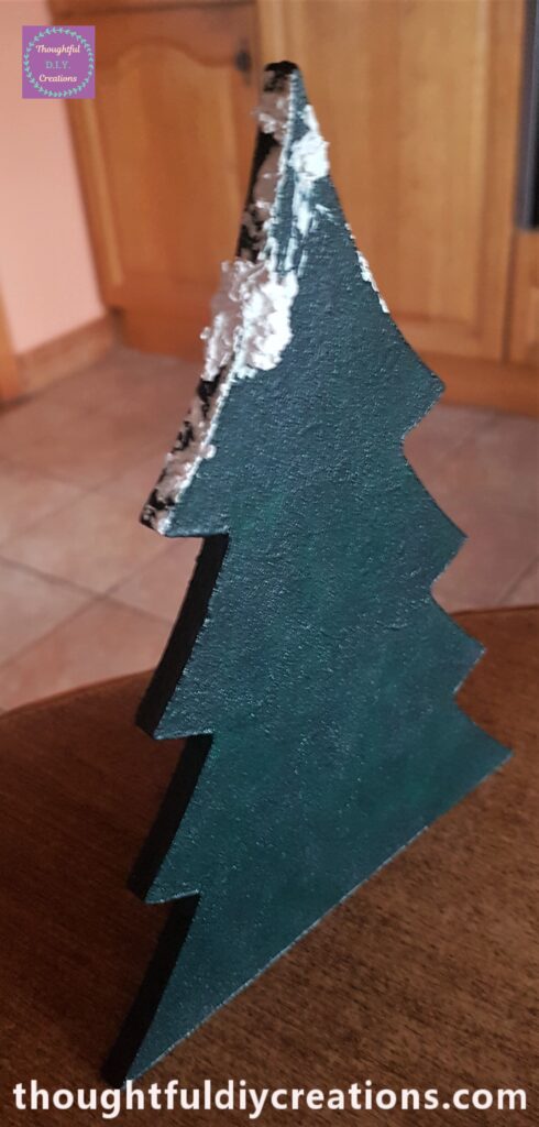 Palette knife dipped into snow paste and spread on the top and sides of the christmas tree.