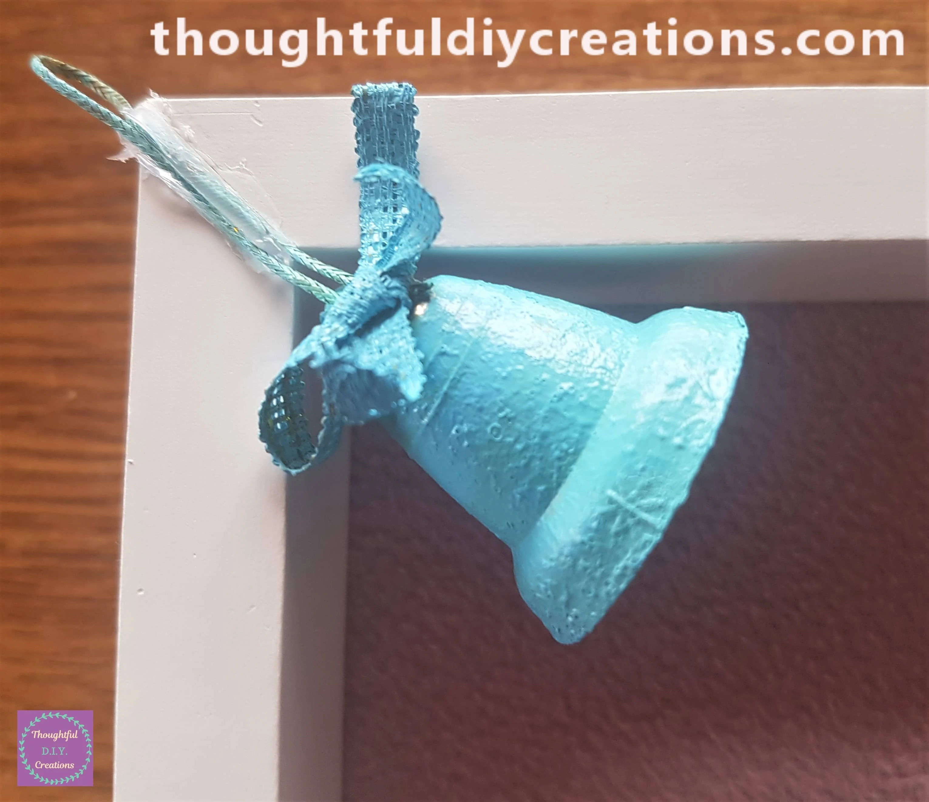 I put Hot Glue on the Top right hand corner of the frame and attached the string of the blue bell into the glue.